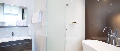 Ein modernes Badezimmer mit einer begehbaren Glasdusche, einer freistehenden Badewanne und einem Waschtisch mit dunkelholzartiger Furnierung.