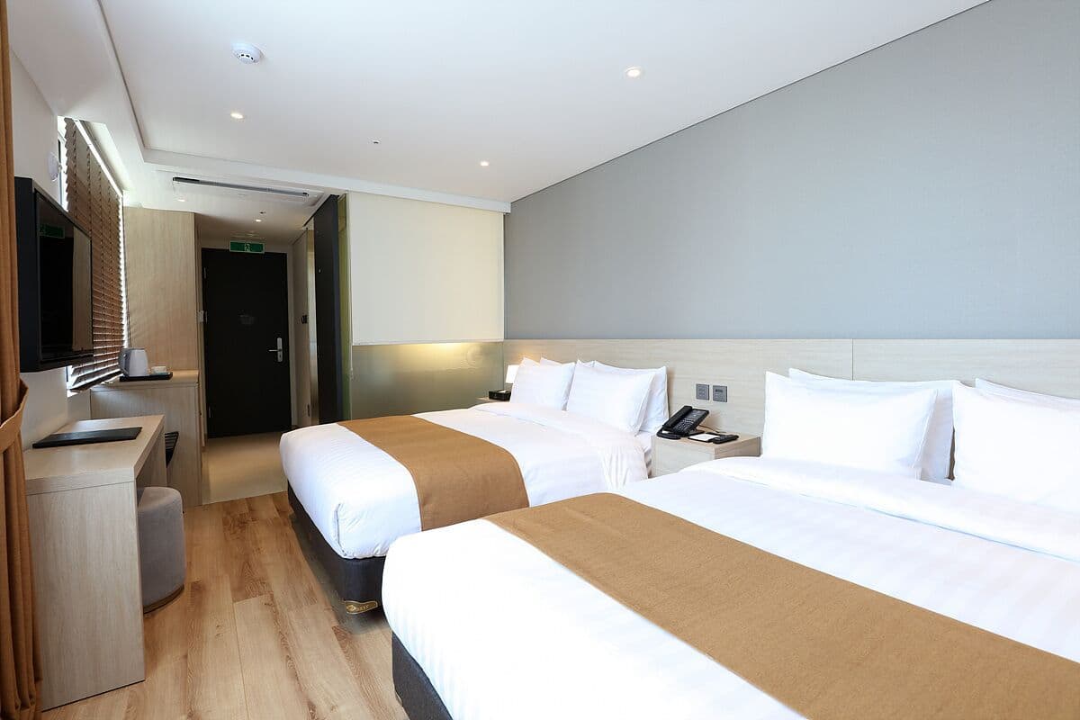 Habitación de hotel con dos camas, un escritorio, un espejo y la puerta del baño.