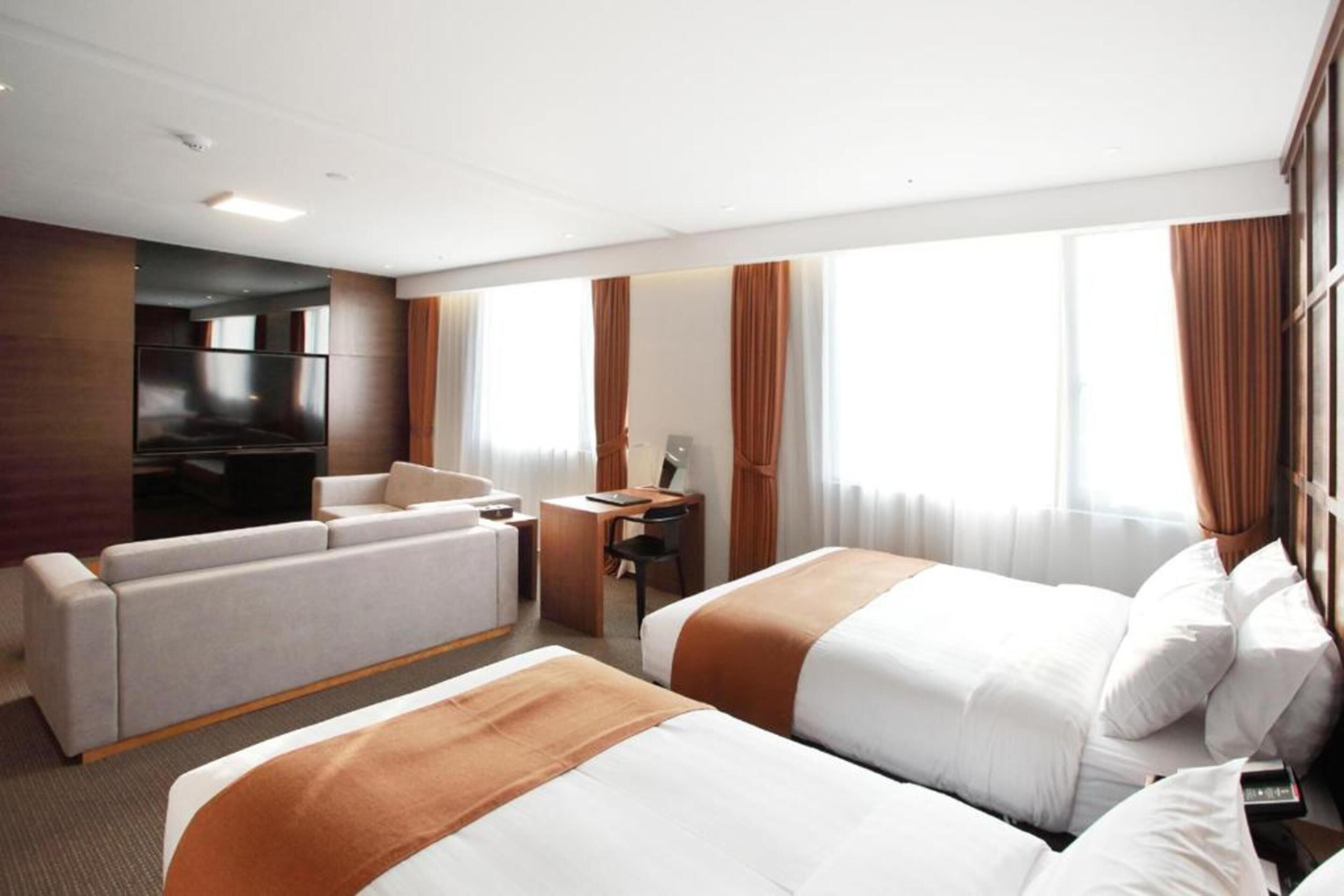 Habitación de hotel con dos camas, un sofá, un escritorio y una televisión.