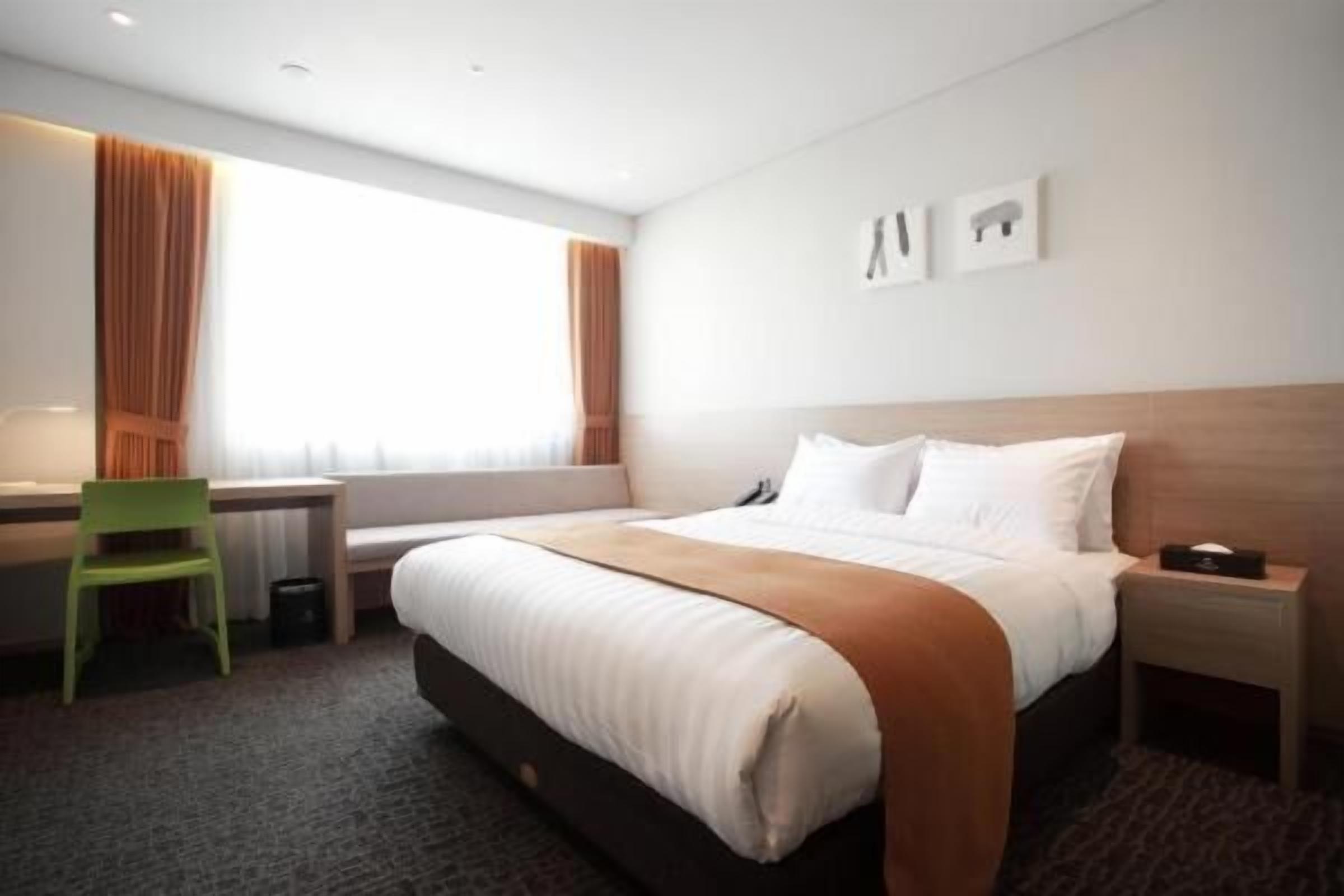 Habitación de hotel con cama, escritorio, silla y ventana con cortinas.