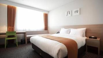 Habitación de hotel con cama, escritorio, silla y ventana con cortinas.