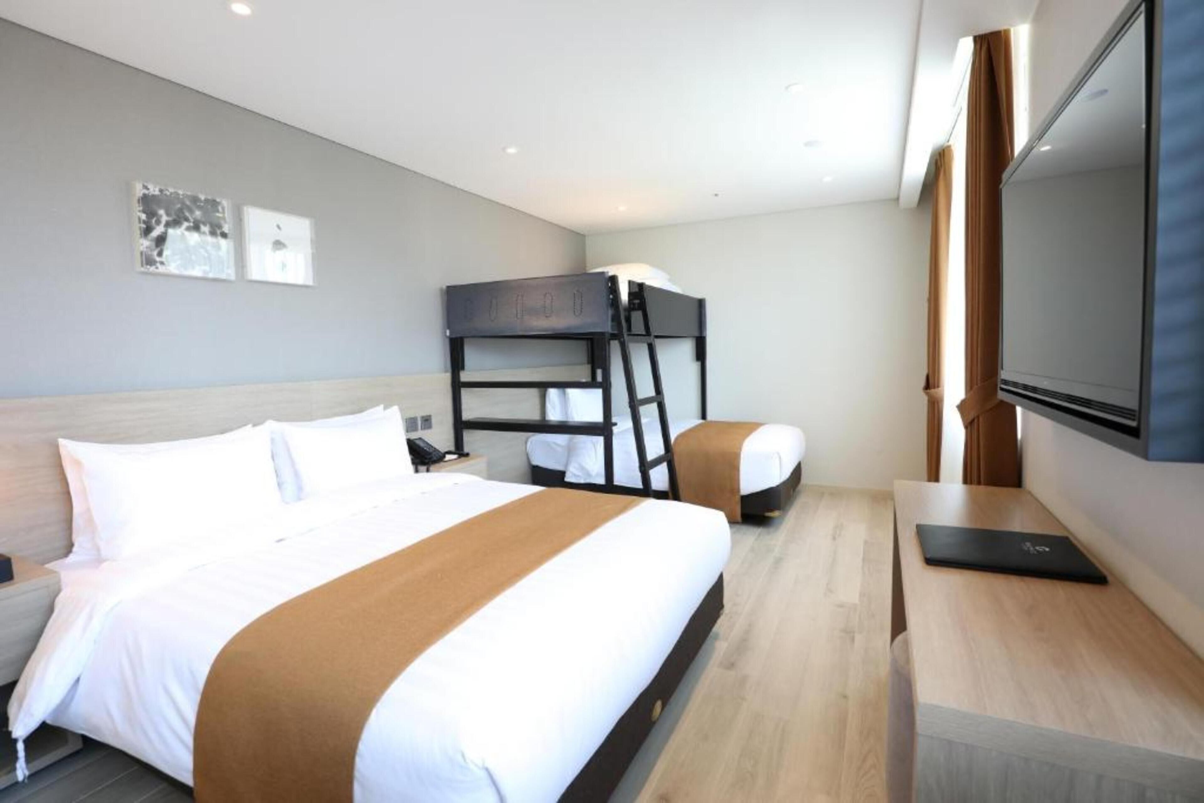 Una habitación de hotel con una cama grande, una litera, un escritorio y un televisor.