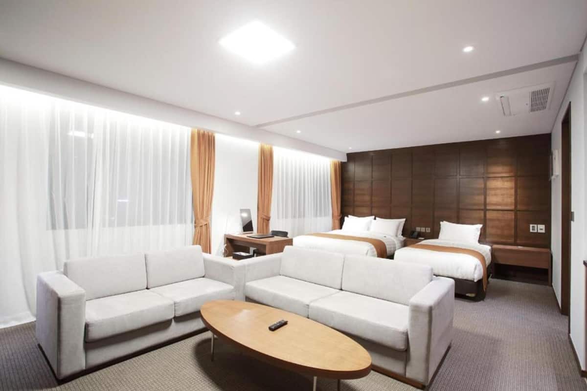Una habitación de hotel moderna con un conjunto de sofás, una cama, una mesita de noche y un ventanal con cortinas.