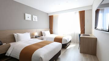 A hotel room with two beds, a bedside table with a lamp, a TV, and a window with curtains.