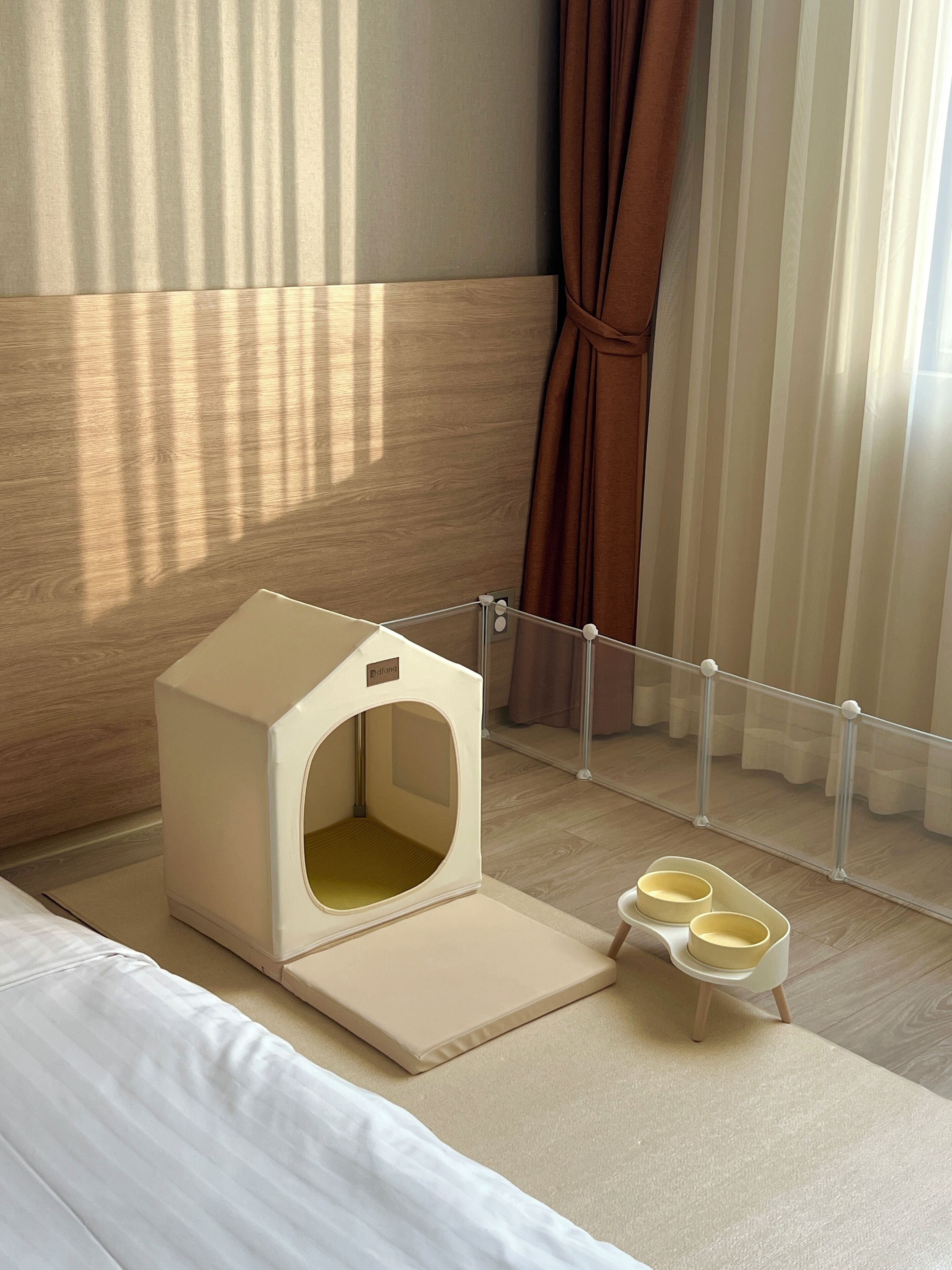 A pet-friendly room with a pet bed, feeding bowls, and a window with curtains.