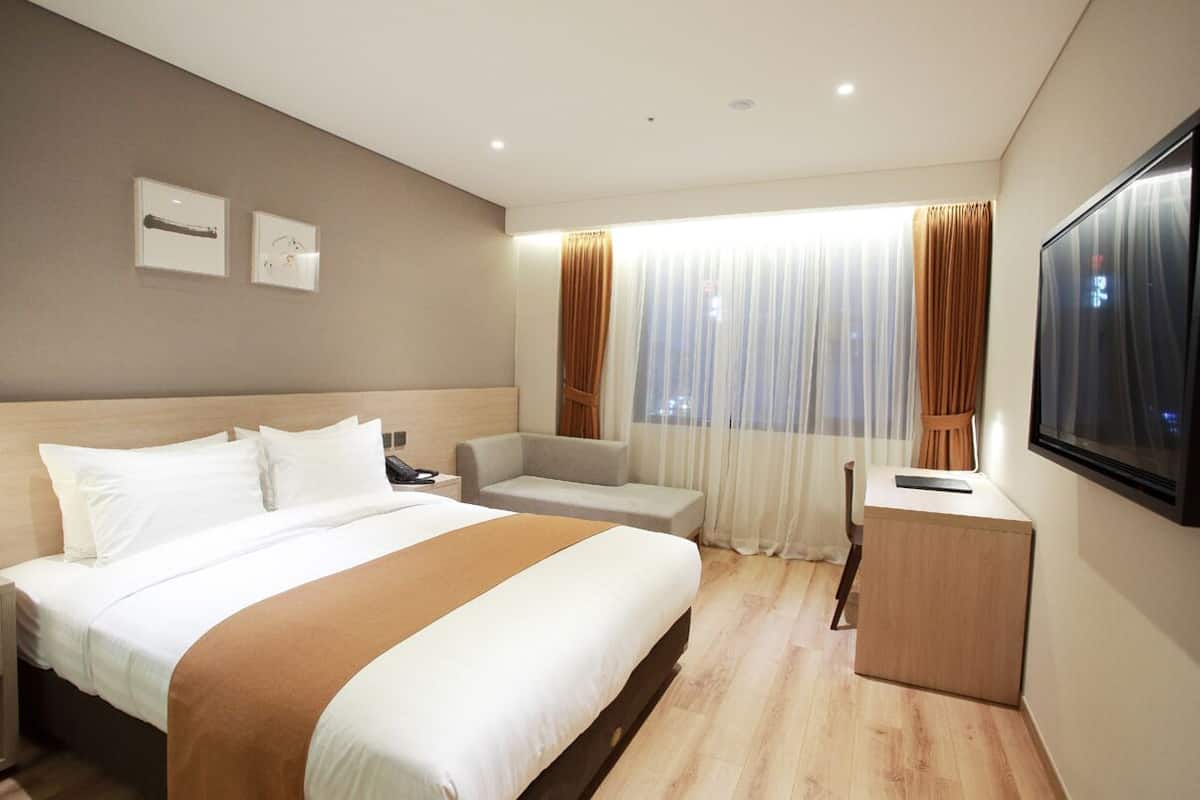 Habitación de hotel con una cama grande, un escritorio, una silla y un televisor instalado en la pared.