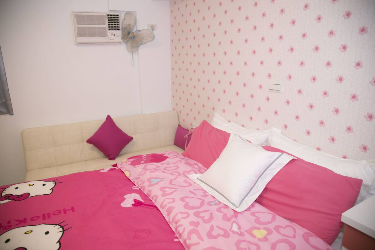 A bedroom with a beige sofa, pink and white patterned bedding, and a Hello Kitty themed bedspread.