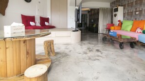 A modern living room with a glass coffee table, red and white sofas, a wooden side table, and a colorful sofa with a toy cart.