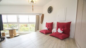 A room with a large window, a round wooden table, and two red cushioned seating areas with Hello Kitty pillows.