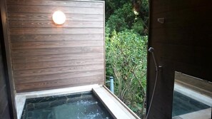 A wooden wall with a circular light fixture and a small outdoor hot tub area with a view of dense greenery. - Hakone Kuranju (Hakone)