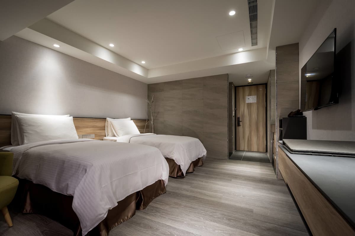 A modern hotel room with two beds, a flat-screen TV, and a wooden cabinet.