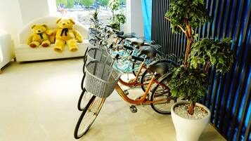 A room with a sofa, a teddy bear, a bicycle with a basket, and a potted plant.