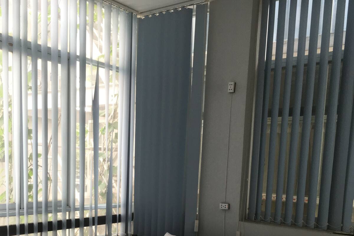A single-bed room with a large window, a wall-mounted power outlet, and a headboard.