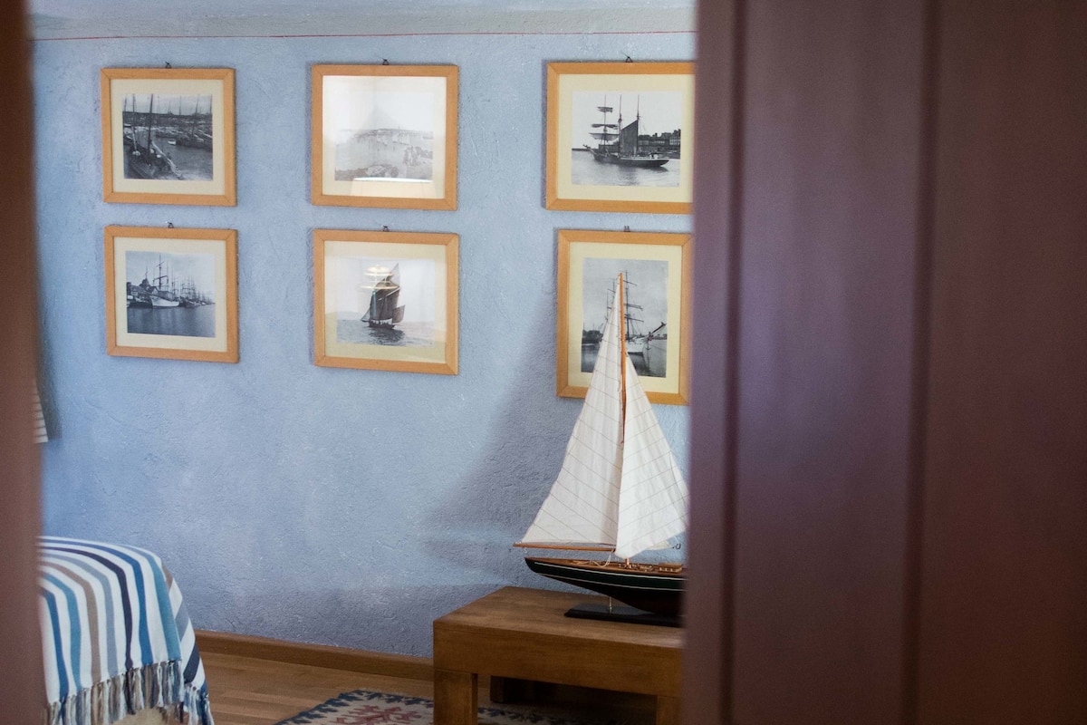 A bedroom with a bed, a rug, a wooden nightstand, and a sailboat model.