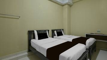 A room with two beds, a small desk, and a shelf with items.