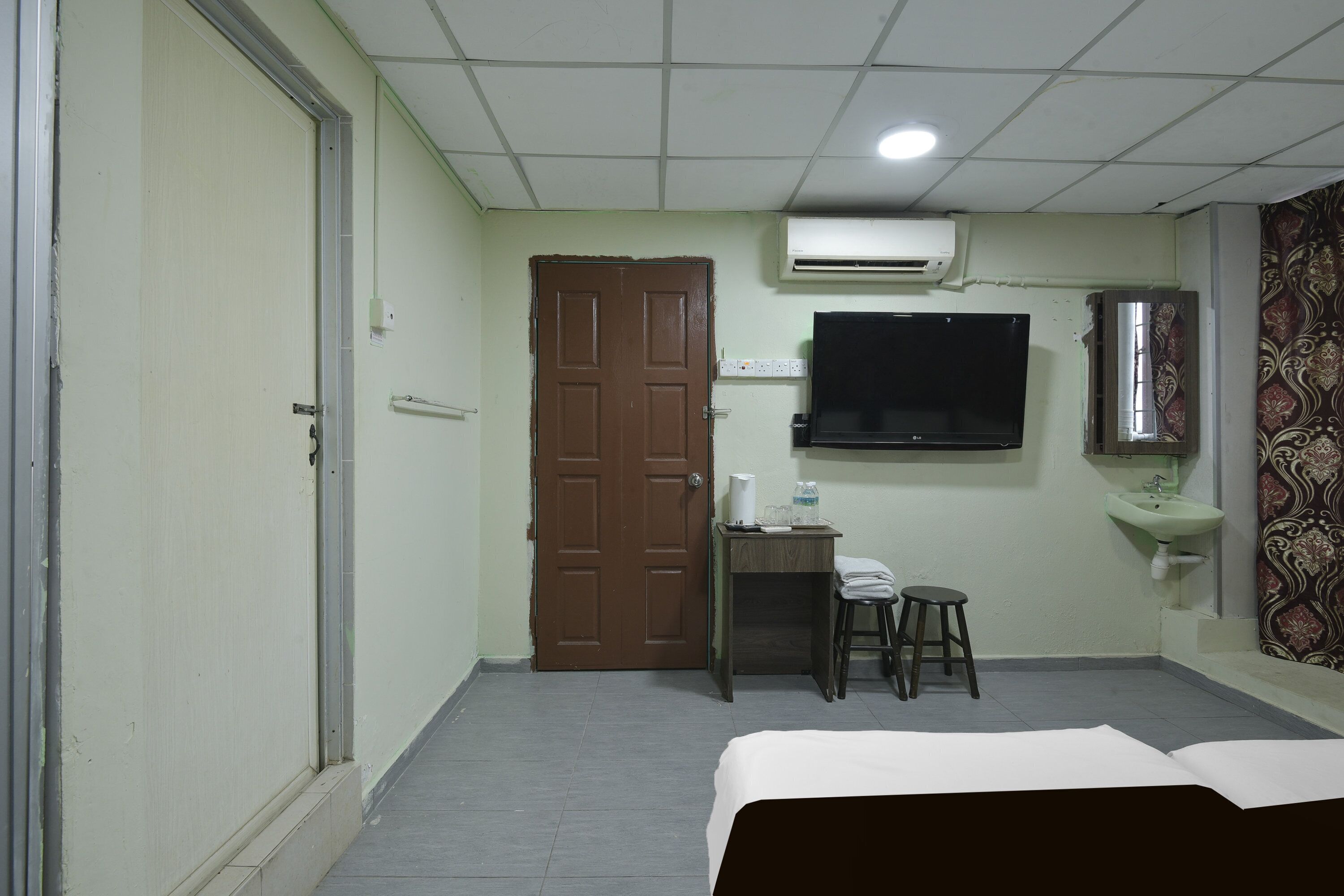 A hotel room with a bed, a desk with a chair, a television, an air conditioner, and a sink.