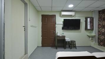 A hotel room with a bed, a desk with a chair, a television, an air conditioner, and a sink.