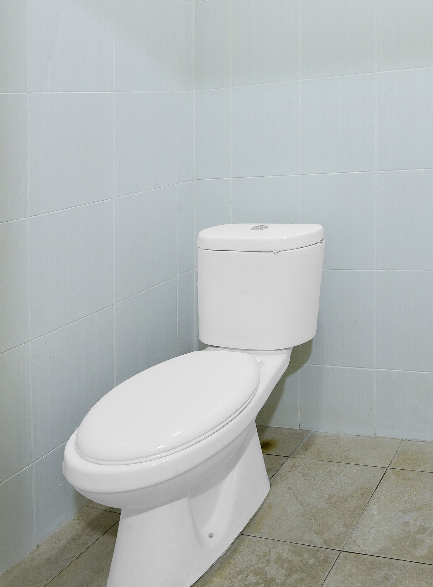 A white toilet in a bathroom with light blue tiled walls and floor.