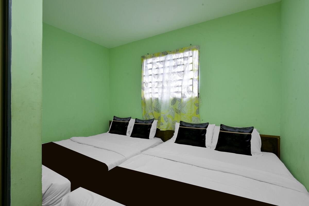 A room with two beds, a window with a leaf-patterned curtain, and green walls.
