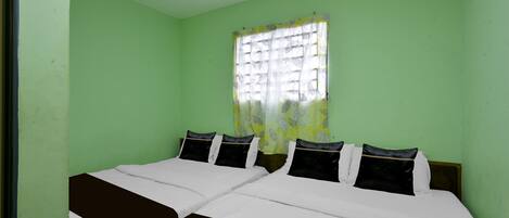 Una habitación con dos camas, una ventana con cortina de motivos vegetales y paredes verdes.