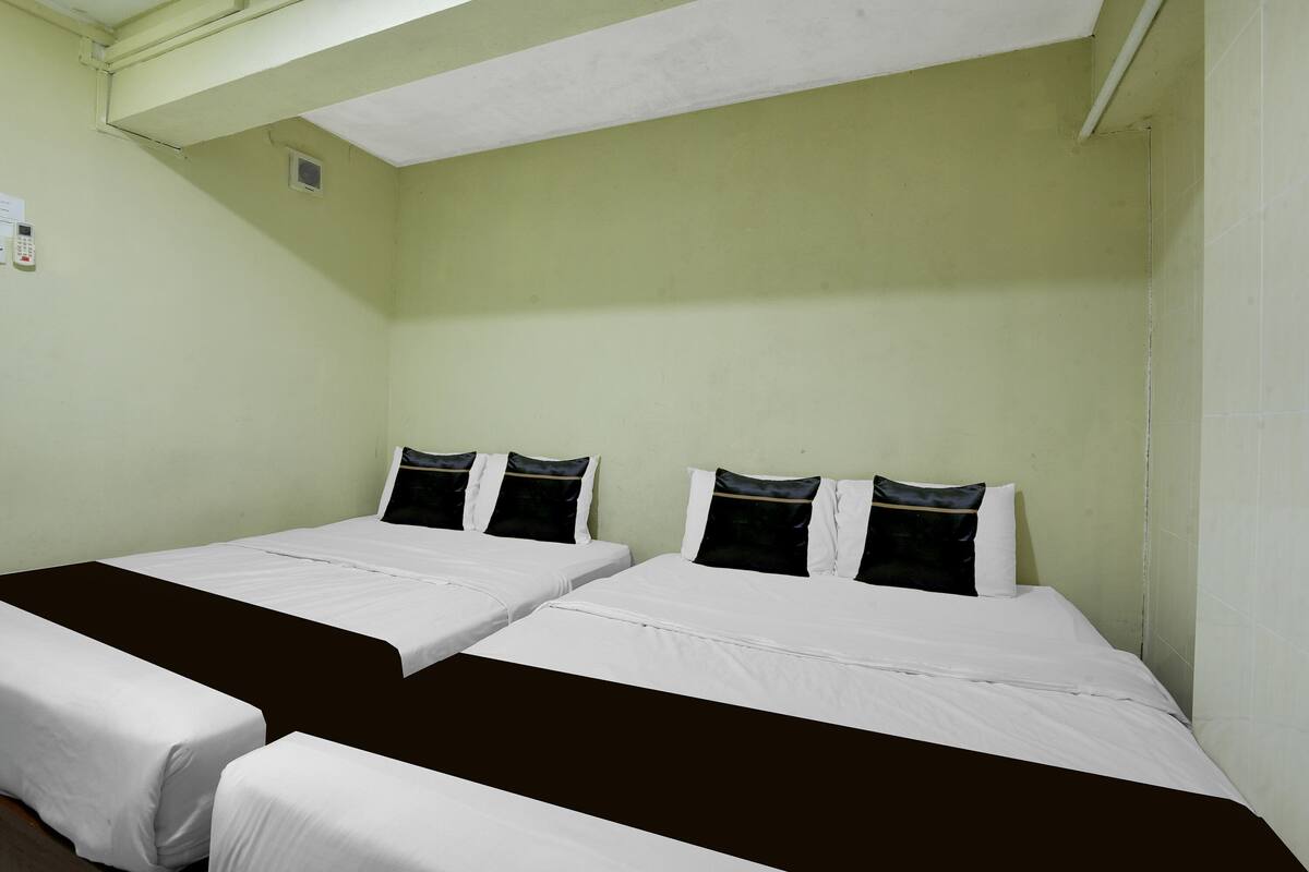 A room with two beds, each with white bedding and black pillows, and a brown bed runner.