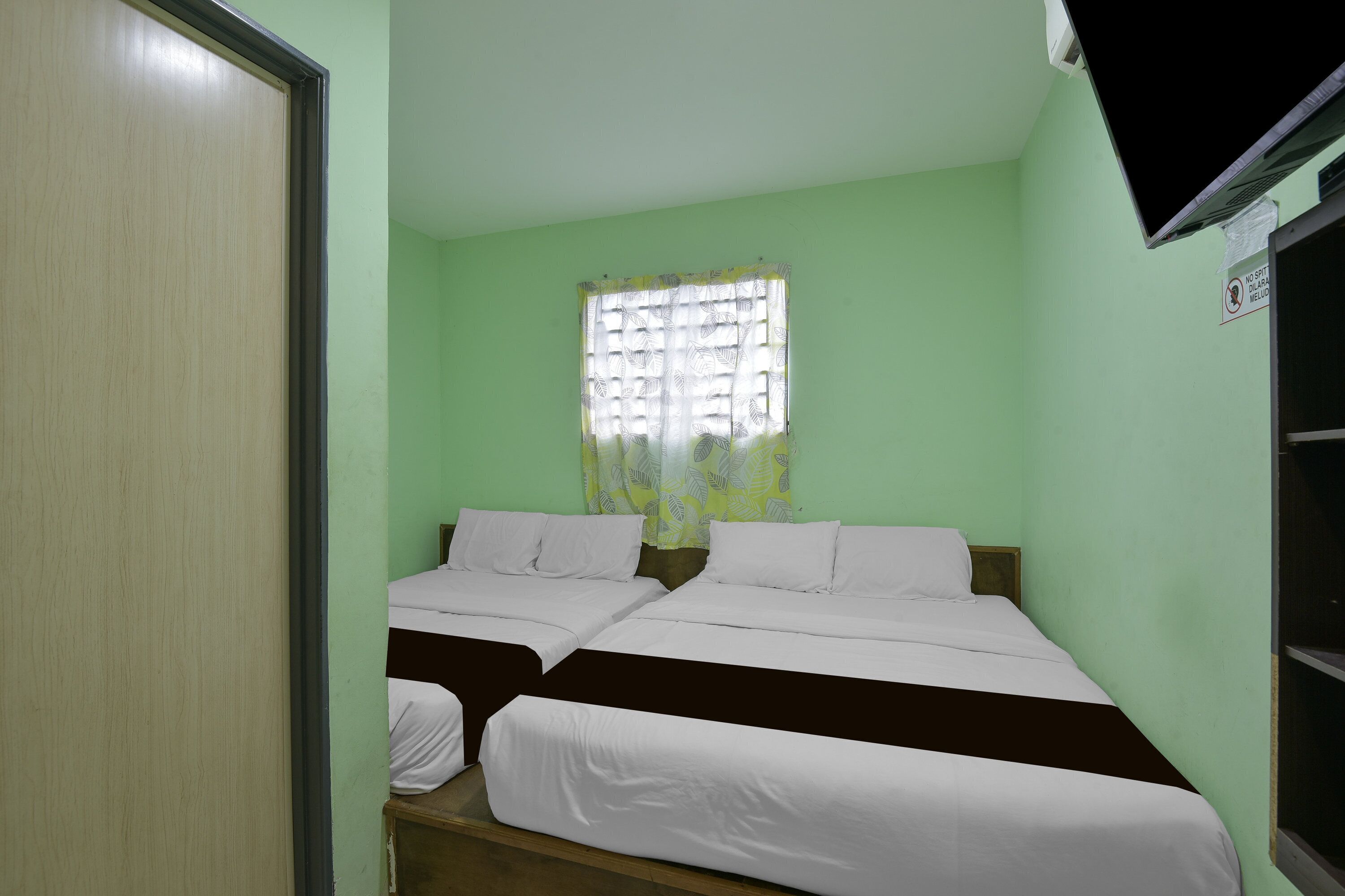 Una habitación con dos camas, una ventana con cortina y un televisor en la pared.