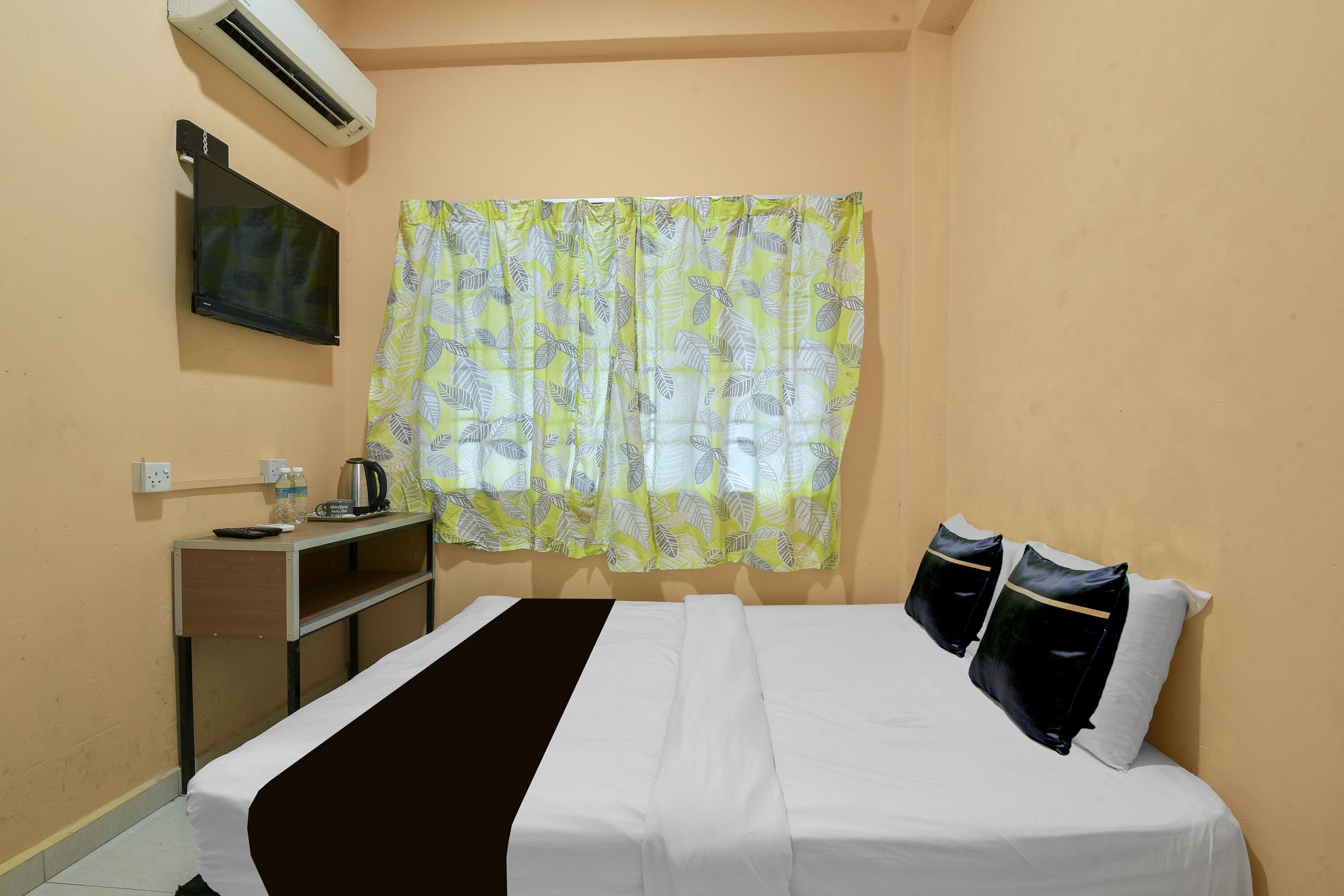 Habitación de hotel con cama, televisor, escritorio con hervidor y ventana con cortinas.