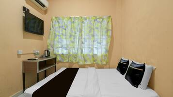 Habitación de hotel con cama, televisor, escritorio con hervidor y ventana con cortinas.