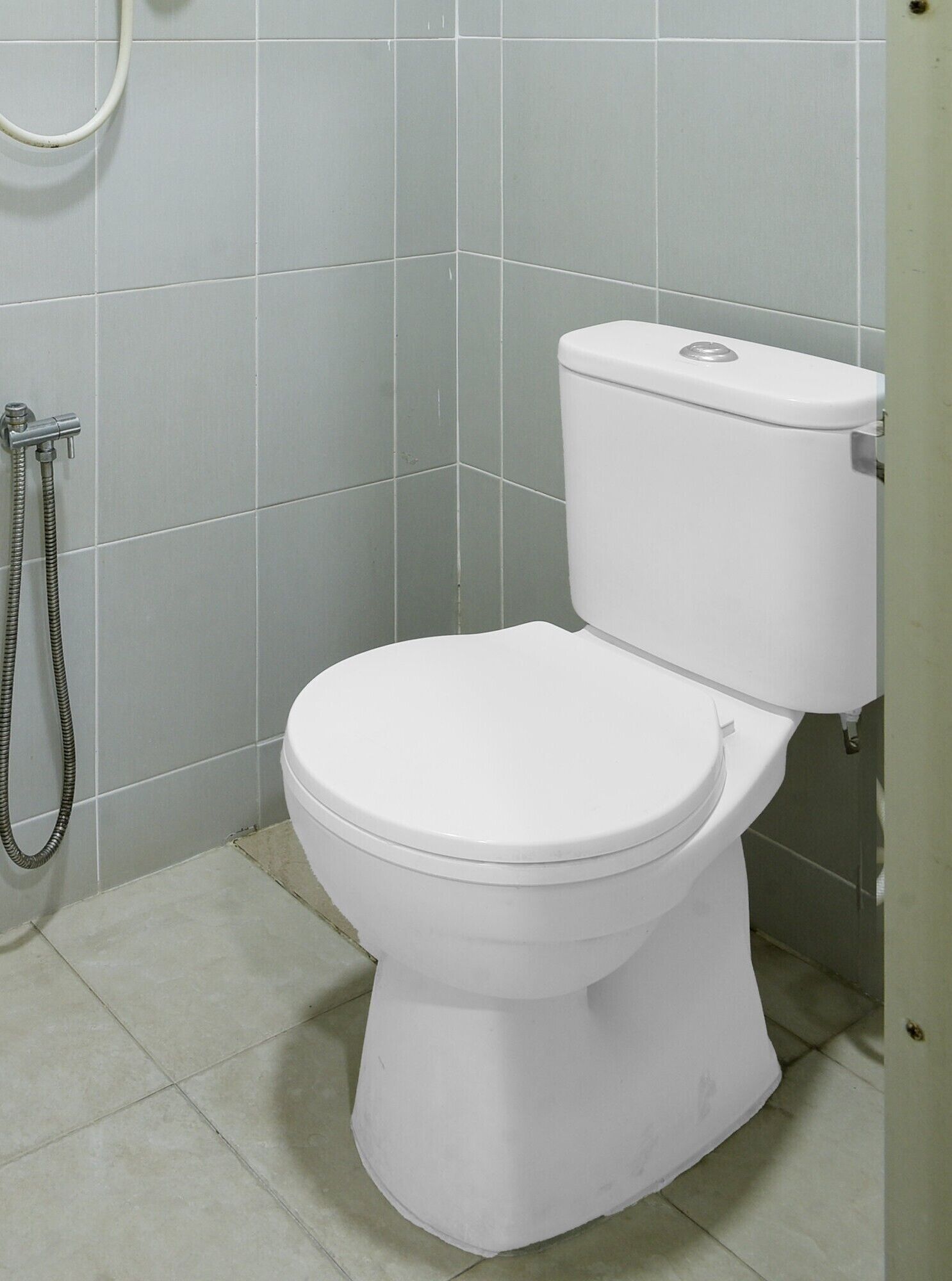 A standard white toilet with a tank, a shower hose, and a tiled floor in a bathroom.