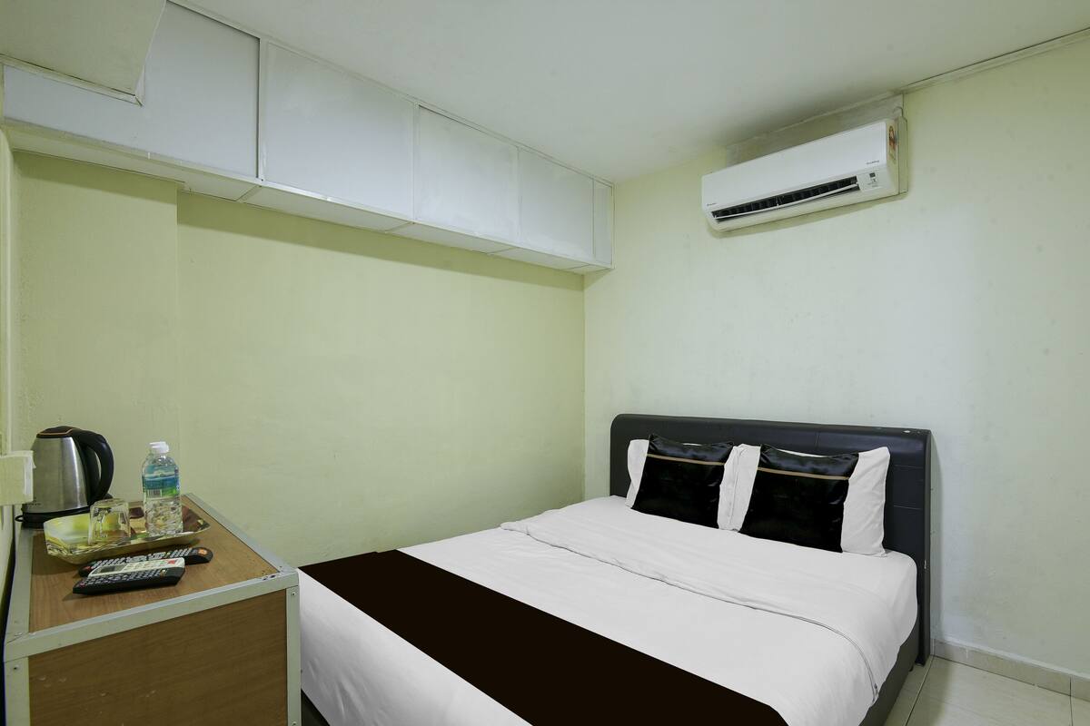 A hotel room with a bed, a desk with a kettle, a water bottle, and a tray with remote controls.