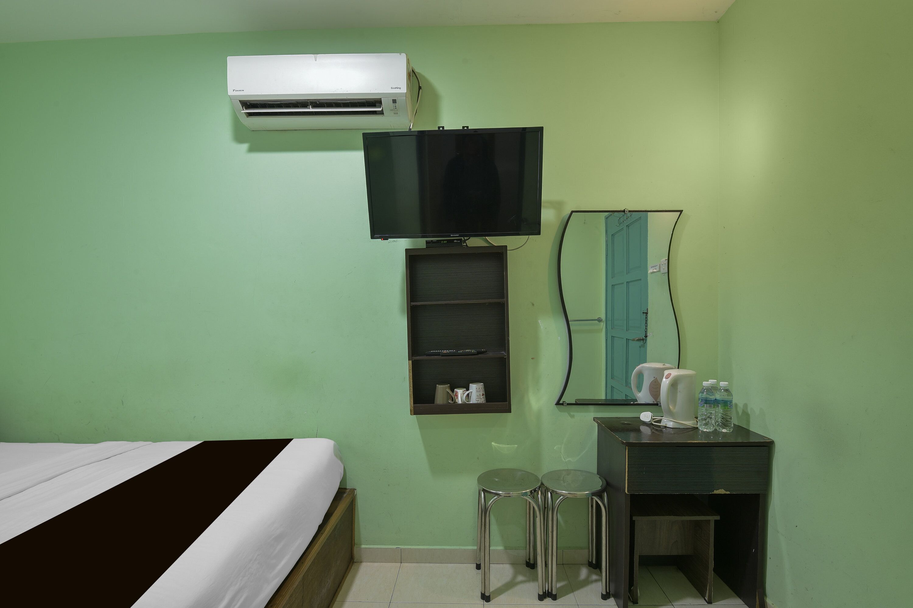 Une chambre comprenant un lit, un bureau avec deux tabourets, un miroir, un climatiseur et un téléviseur.