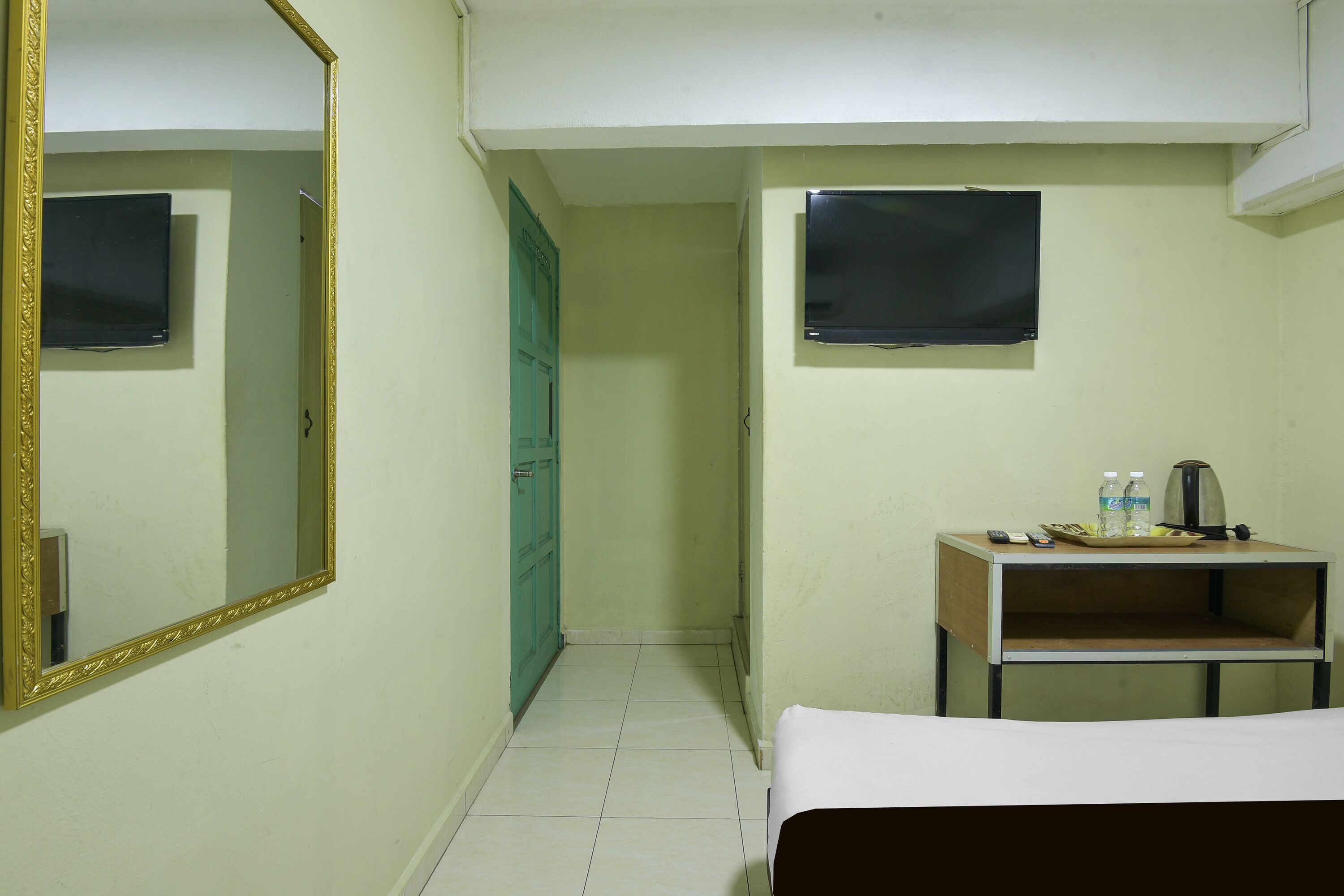 Una habitación de hotel con una cama, un pequeño escritorio con un hervidor, dos botellas y un control remoto.