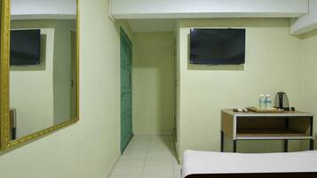 Una habitación de hotel con una cama, un pequeño escritorio con un hervidor, dos botellas y un control remoto.