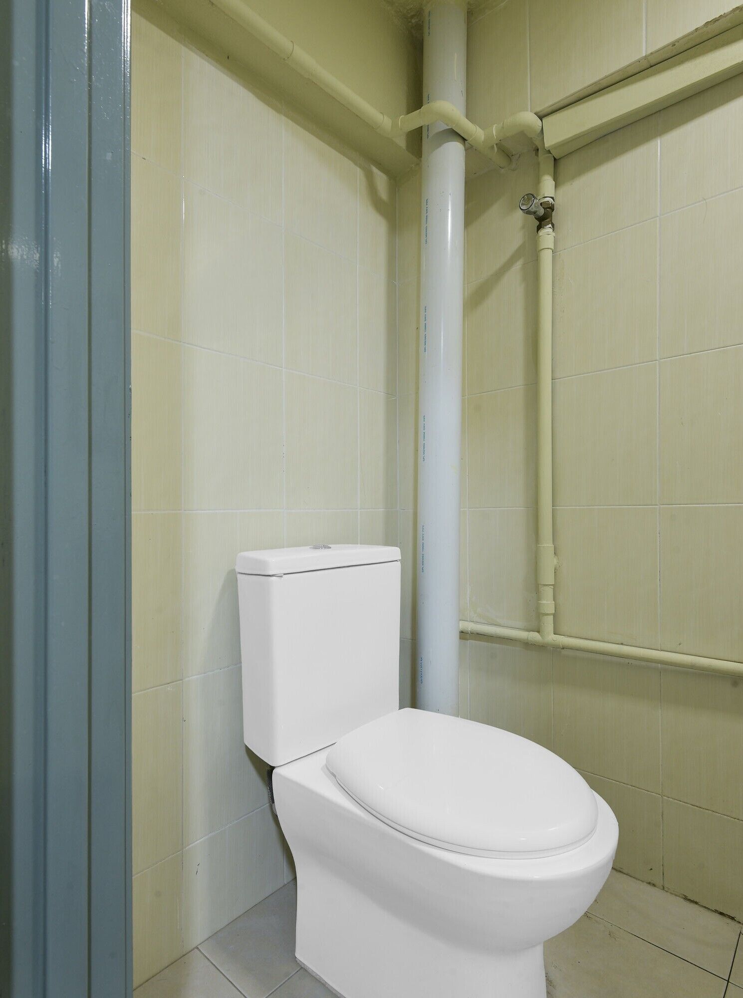 Un inodoro blanco en un baño con paredes de azulejos y una estructura de tuberías visible.
