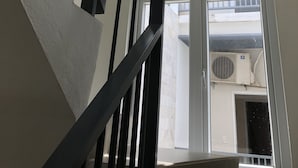A staircase with black railings leading to a balcony with a view of an air conditioning unit and a door. - Homestay Des Amis - Ban Huu (Da Nang)