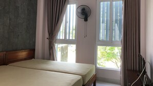 A room with two beds, a window with curtains, a standing fan, and an air conditioning unit. - Homestay Des Amis - Ban Huu (Da Nang)
