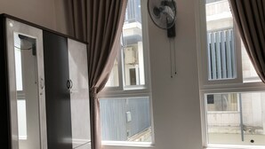 A room with a large wardrobe, a standing fan, and multiple windows allowing natural light. - Homestay Des Amis - Ban Huu (Da Nang)