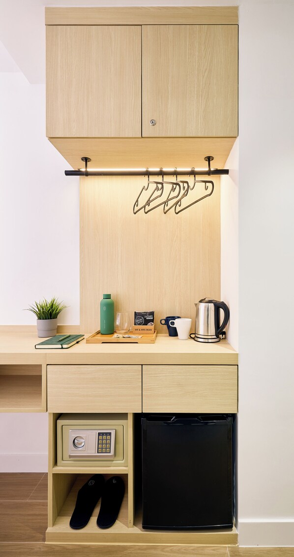 A compact kitchen with wooden cabinetry, a coffee maker, a kettle, and a small refrigerator.