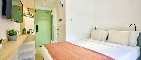 A modern hotel room with a large bed, a desk with drawers, a mirror, and a green door.