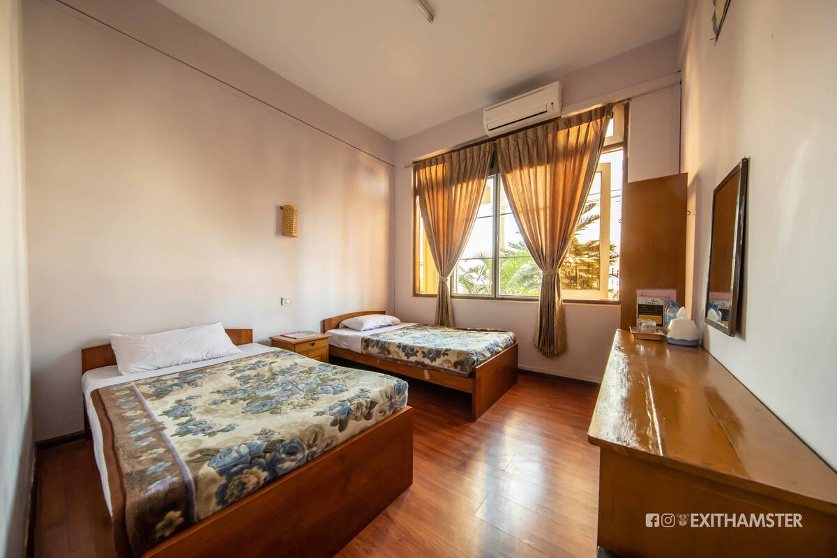 A hotel room with two wooden beds, a wooden desk, a mirror, and a window with curtains.