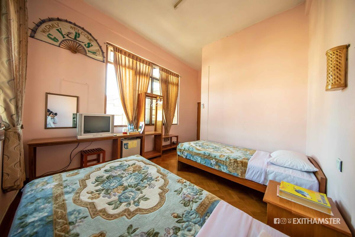 A room with two beds, a desk with a computer, and a window with curtains.