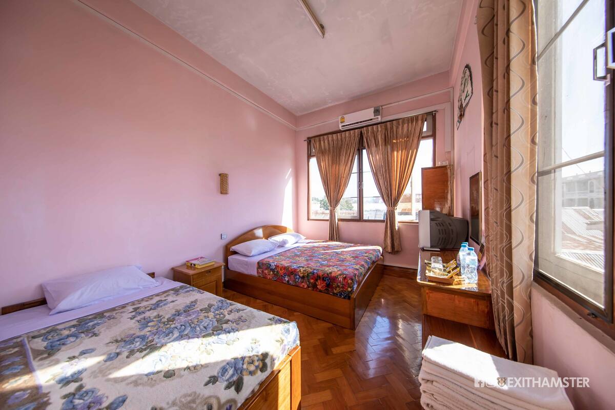 A bedroom with two beds, a wooden nightstand, a desk with a computer, and a window with curtains.