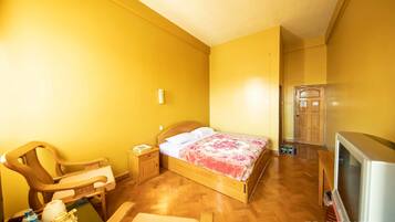 A room with a wooden bed, a chair, a small table, a television, and a door.