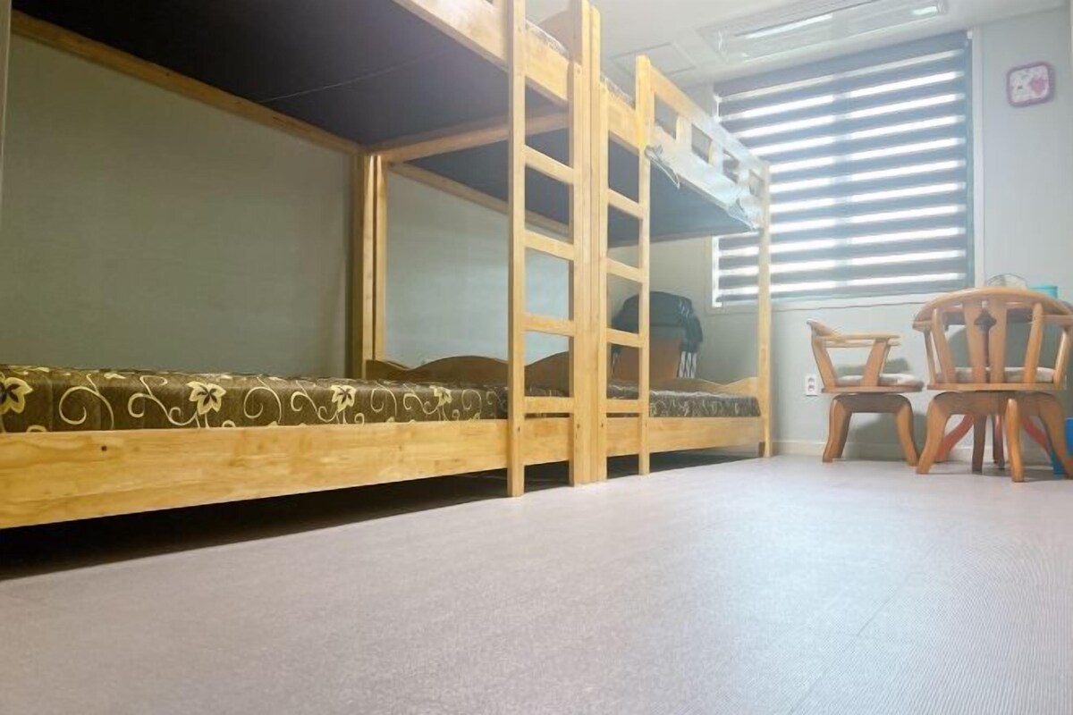 A bunk bed with a ladder, a small table, and two chairs in a room with a window and blinds.
