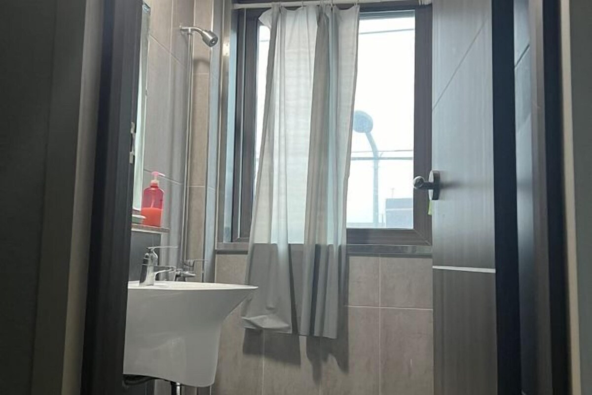 A bathroom with a sink, a shower, and a window with curtains.