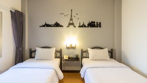 Quarto de hotel com duas camas, uma luminária fixada na parede e um mural com vista para a cidade.