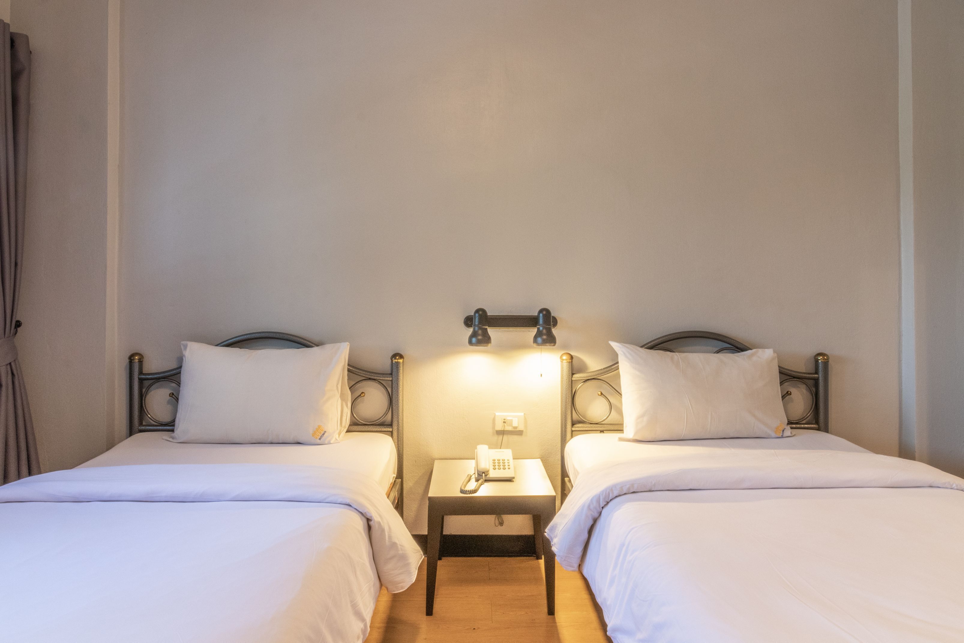 Une chambre d’hôtel avec deux lits simples, une petite table de chevet avec un téléphone et un luminaire fixé au mur.