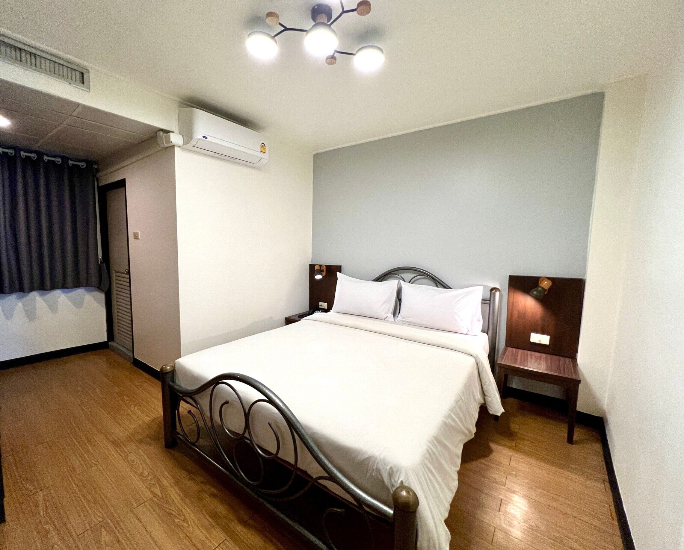Une chambre d’hôtel équipée d’un lit, d’une table de chevet, d’un climatiseur fixé au mur et d’un luminaire au plafond.