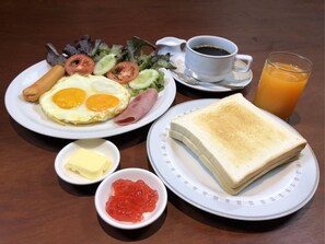 A breakfast plate with eggs, ham, and vegetables, a cup of coffee, a glass of orange juice, butter, and jam.