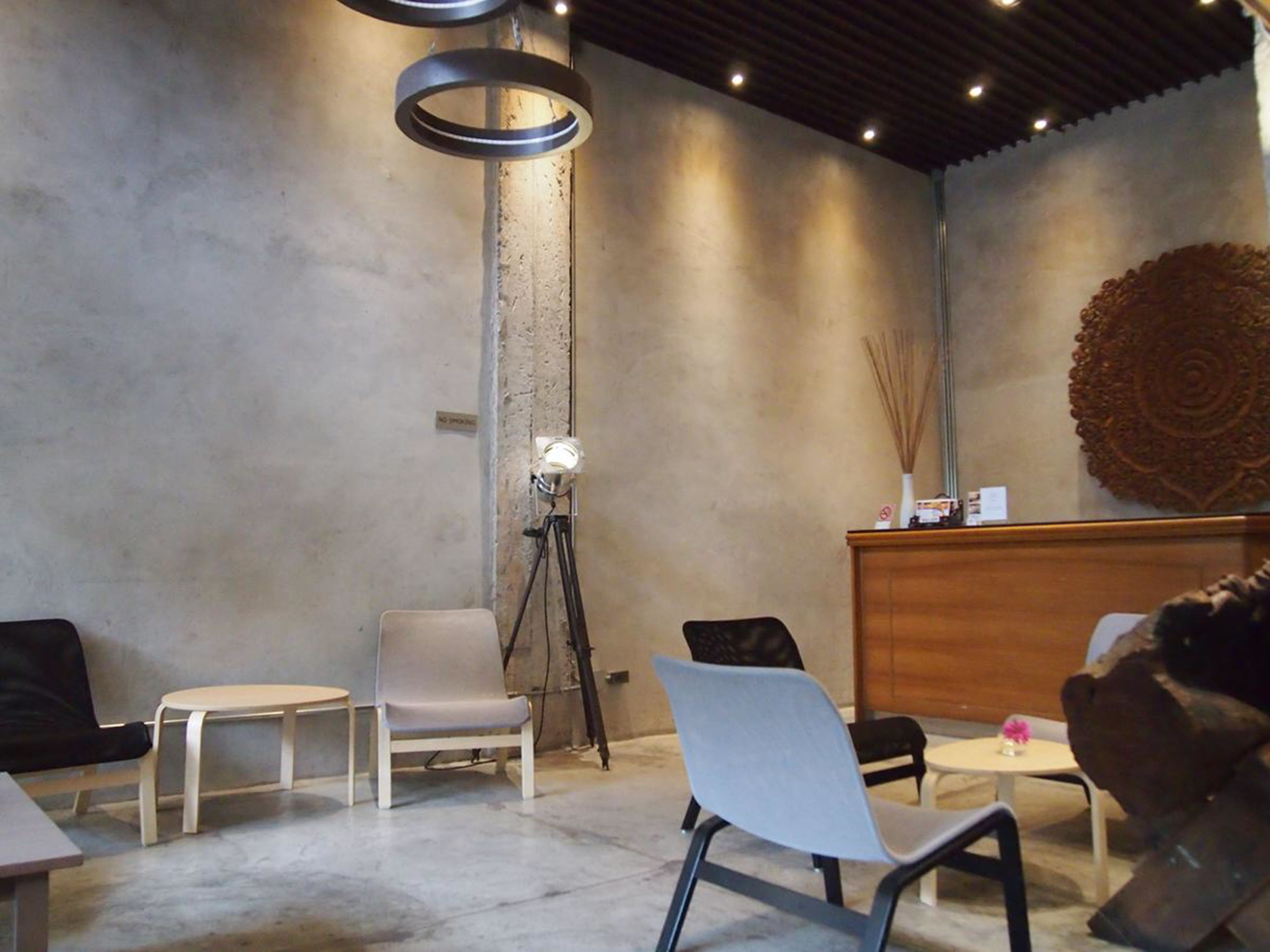 A modern interior with a concrete wall, a wooden reception desk, and a large decorative wall piece. There are several chairs and tables arranged for seating.